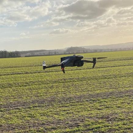 drone hovering Black drone hovering above a green field under a cloudy sky.