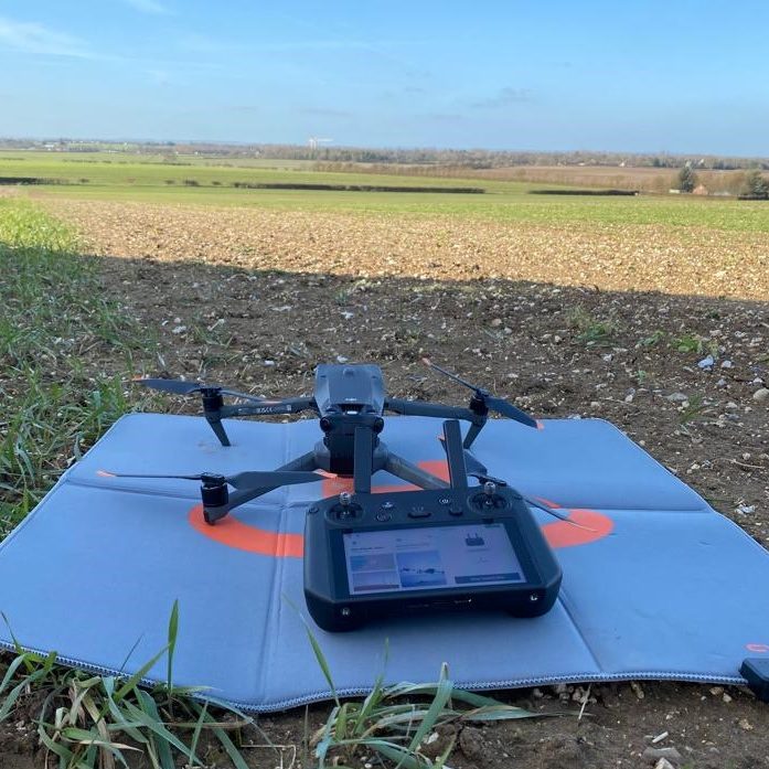 DJI Mavice 3M Drone on a launch pad with a controller, set in a rural landscape under a clear blue sky.